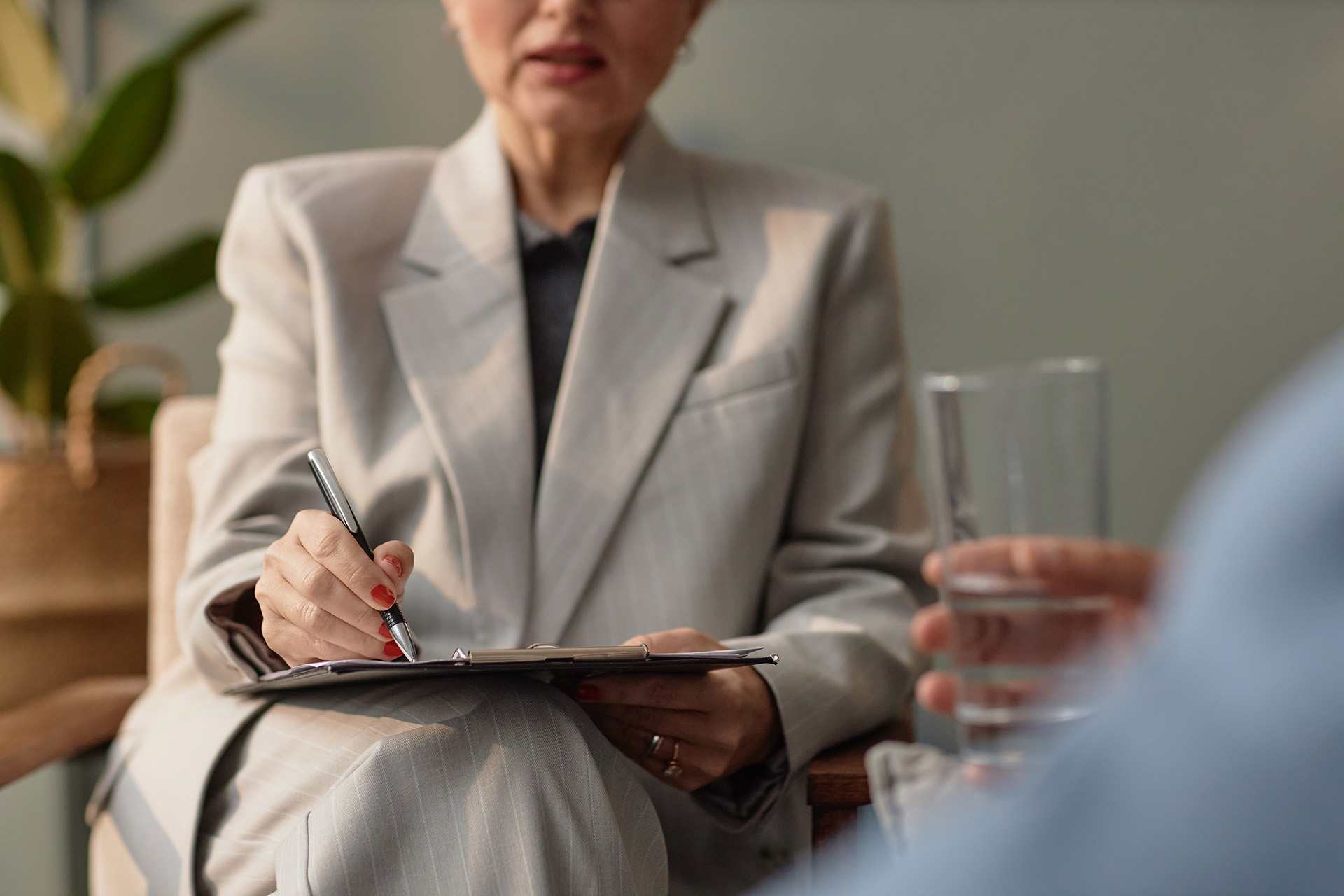 Person sitzt bei einer Beratung zur verkehrspsychologischen Einzelintervention einer Frau in Anzug und Clipboard gegenüber.